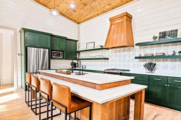 Island with leather stools, green cabinets and a wood range hood