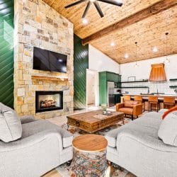 Great room with a stone fireplace to the ceiling, a green accent wall and gray armchairs