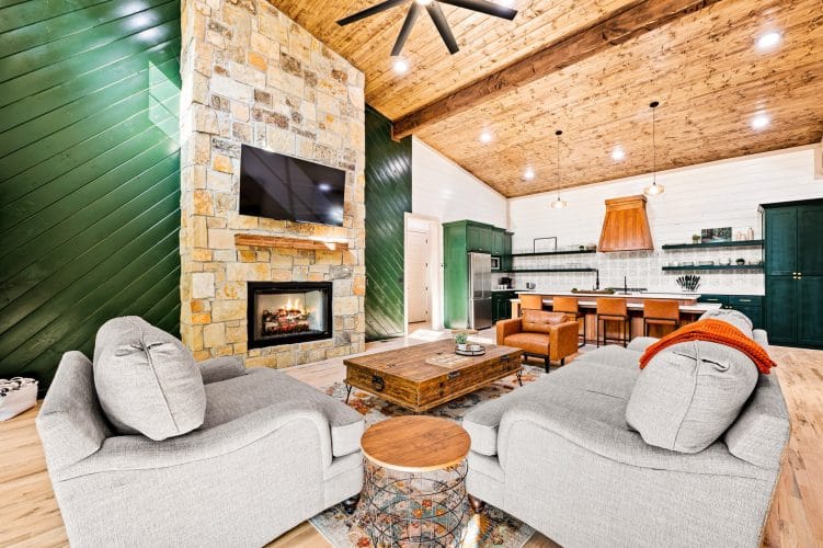 Great room with a stone fireplace to the ceiling, a green accent wall and gray armchairs