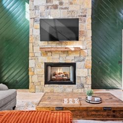 Stone fireplace with a TV above it, green accent walls and a wood coffee table