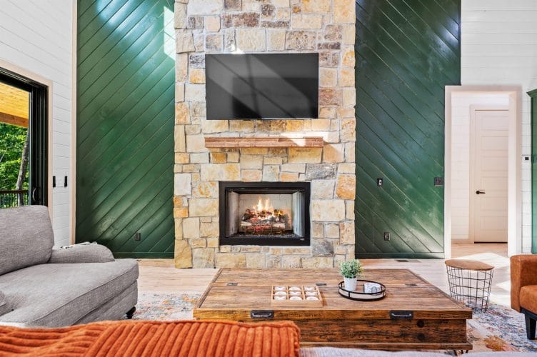 Stone fireplace with a TV above it, green accent walls and a wood coffee table