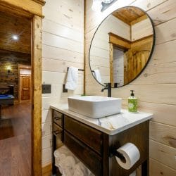 Vessel sink vanity with a round mirror, game room visible through the door
