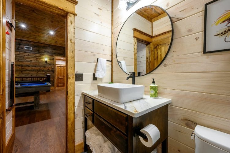 Vessel sink vanity with a round mirror, game room visible through the door