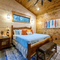 King bed with a light blue cover and orange pillows on a live-edge wood bed