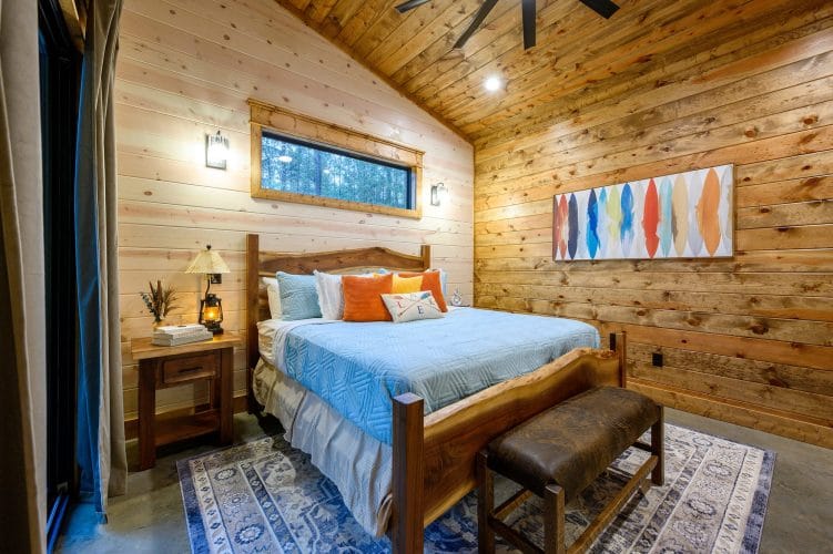 King bed with a light blue cover and orange pillows on a live-edge wood bed