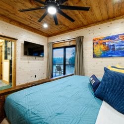 King bed with teal cover and a TV, window looking out toward the water