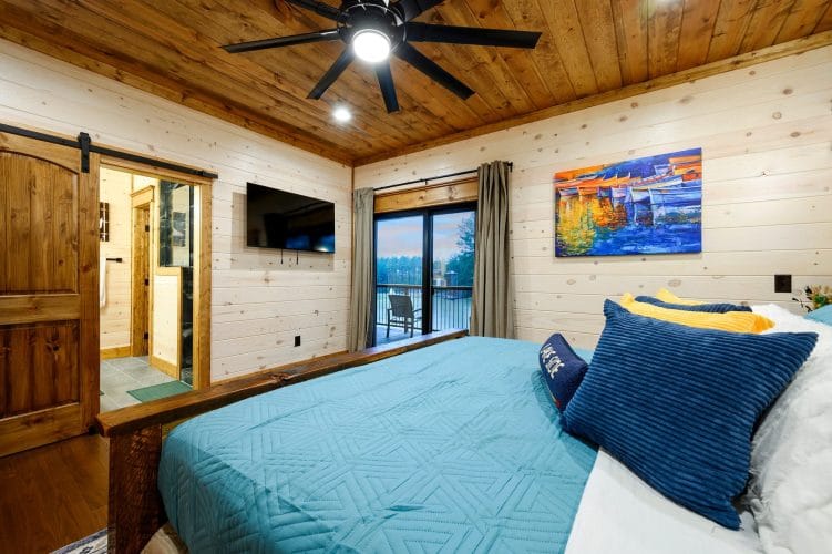 King bed with teal cover and a TV, window looking out toward the water