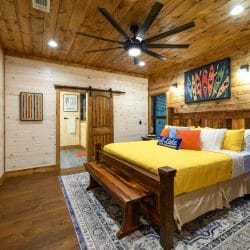 Wood-frame king bed with a yellow cover, bench at the foot and a barn door
