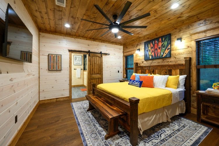 Wood-frame king bed with a yellow cover, bench at the foot and a barn door