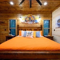 King bed with an orange cover against a wood wall with boat art
