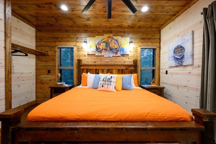King bed with an orange cover against a wood wall with boat art