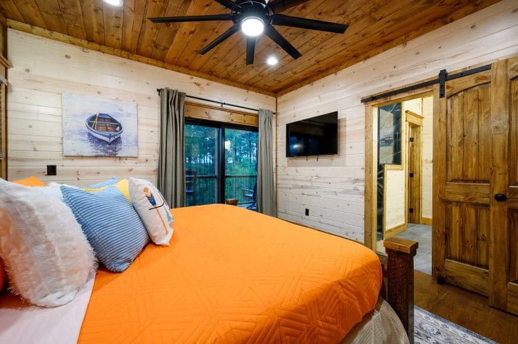 King bed with orange cover, ceiling fan, TV and sliding door