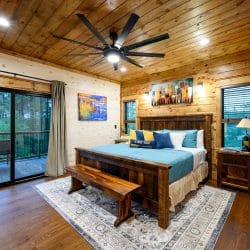 King bed with a teal cover and bench at the foot, sliding doors to a deck