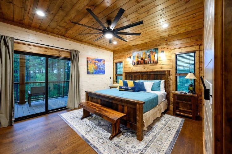 King bed with a teal cover and bench at the foot, sliding doors to a deck