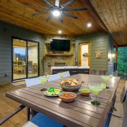 Covered deck with a dining table and a stone fireplace with TV