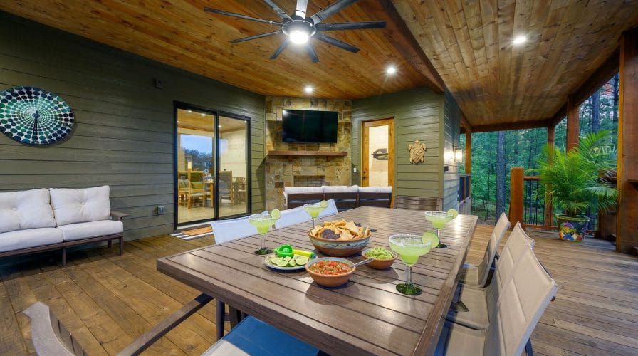Covered deck with a dining table and a stone fireplace with TV
