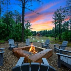 Fire burning in a rectangular fire pit with Adirondack chairs, water behind