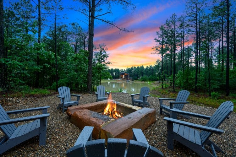 Fire burning in a rectangular fire pit with Adirondack chairs, water behind