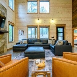 Two-story living room with a black leather sectional, tan leather chairs and a stone fireplace