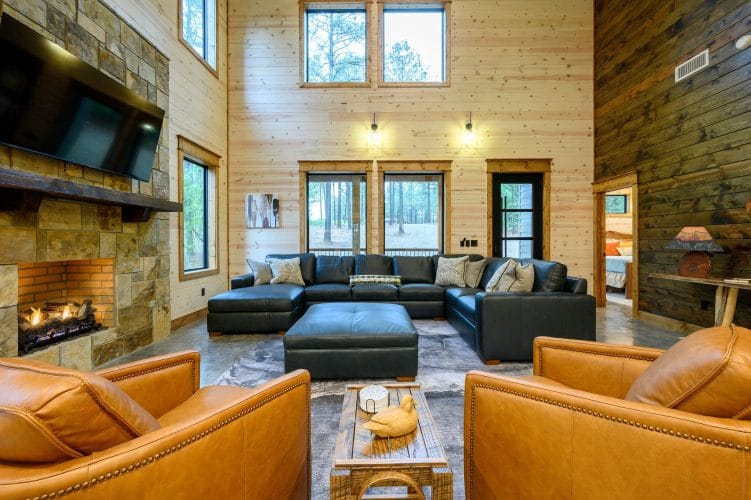 Two-story living room with a black leather sectional, tan leather chairs and a stone fireplace