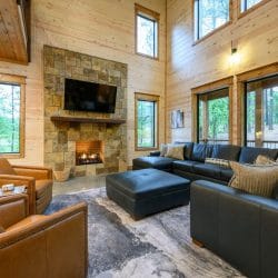 Living room with leather chairs, sectional and stone fireplace under tall windows