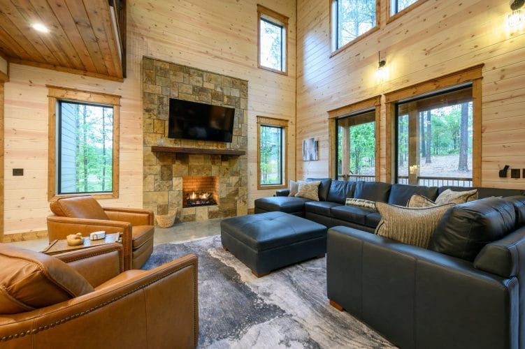 Living room with leather chairs, sectional and stone fireplace under tall windows