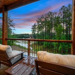 Two lounge chairs on a deck looking out over pines and the water at dusk