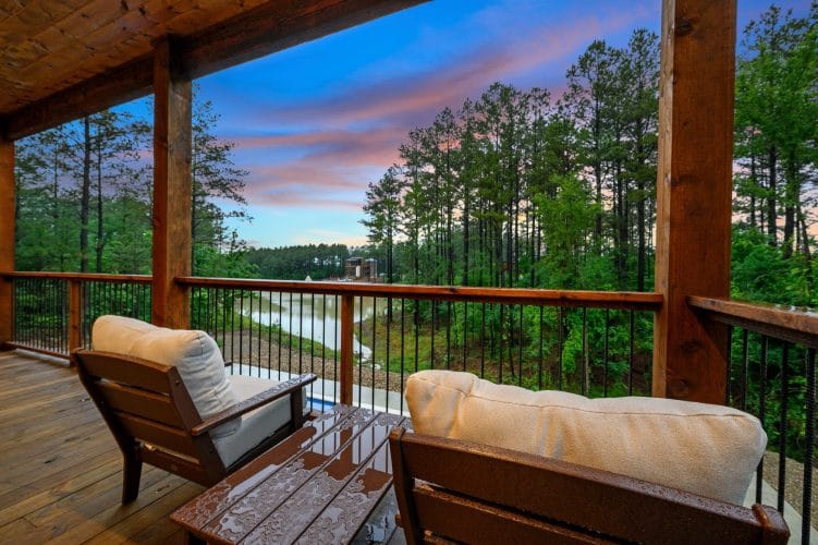 Two lounge chairs on a deck looking out over pines and the water at dusk