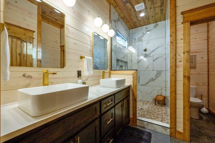 Double vessel-sink vanity next to a marble-look shower