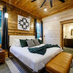 King bed with white bedding, green throw and a leather bench at the foot