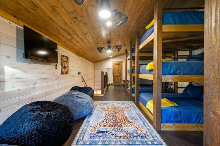 Row of triple-stacked bunks with a wall TV and bean bag chairs