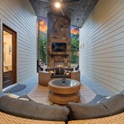 Round sectional sofa facing a stone fireplace with a TV on the covered patio