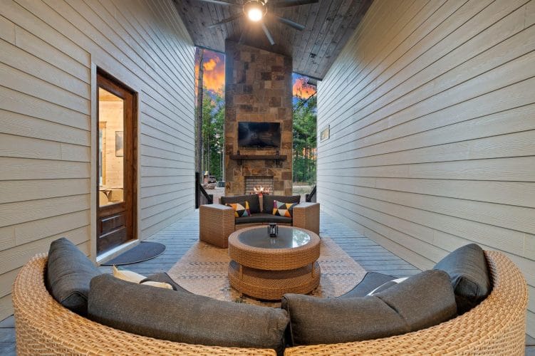 Round sectional sofa facing a stone fireplace with a TV on the covered patio