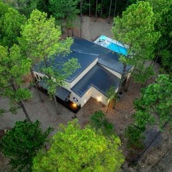 Aerial view of the house roof among tall pines with the pool beside it