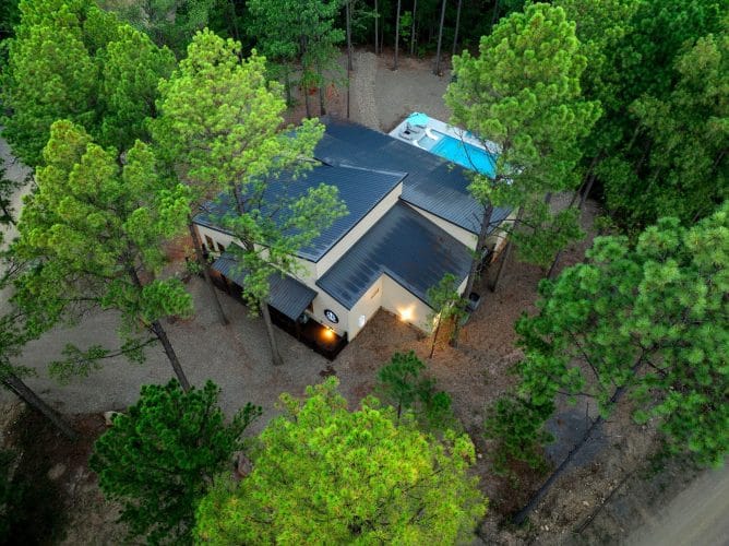 Aerial view of the house roof among tall pines with the pool beside it