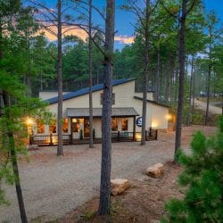 House with a lit front porch among tall pines at dusk