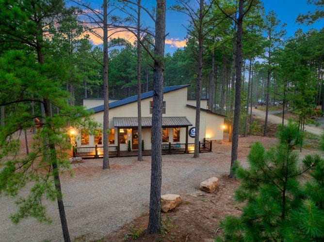 House with a lit front porch among tall pines at dusk