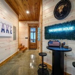 Game room hall with a bar-height table and a neon 'The Gather House' sign