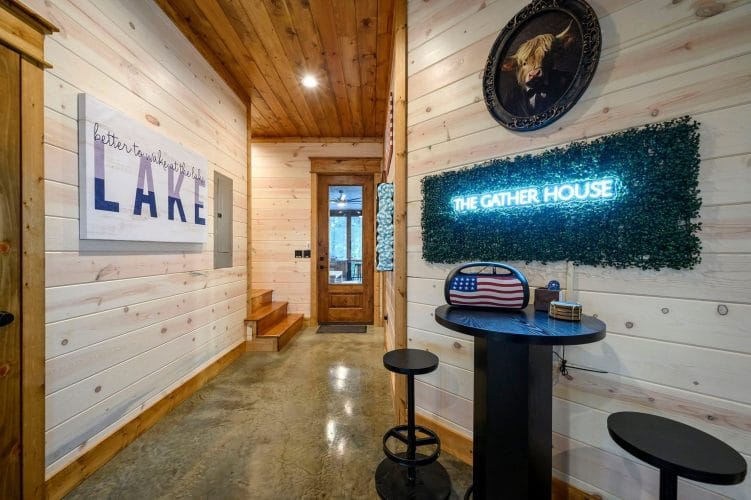 Game room hall with a bar-height table and a neon 'The Gather House' sign