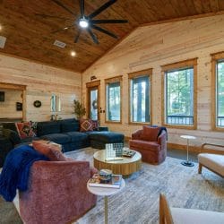 Sectional, rose armchairs and a round coffee table beside windows onto the pines