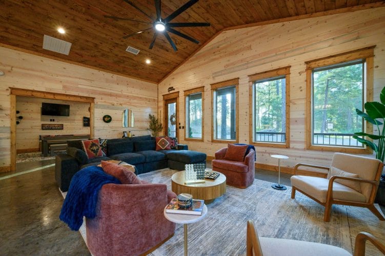 Sectional, rose armchairs and a round coffee table beside windows onto the pines