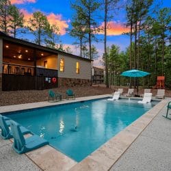 Rectangular pool with in-water loungers and a lit covered porch behind it at dusk