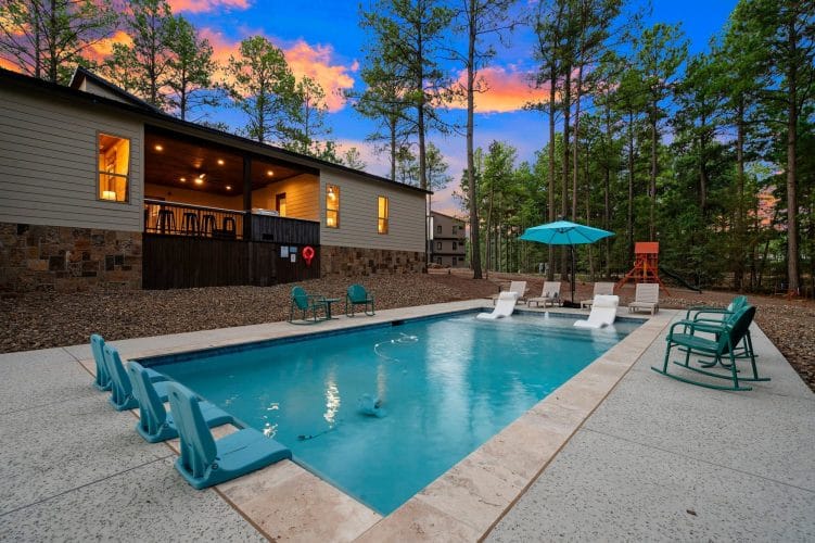 Rectangular pool with in-water loungers and a lit covered porch behind it at dusk