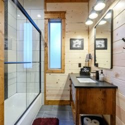 Bathroom vanity with a dark counter beside a narrow window and a glass shower