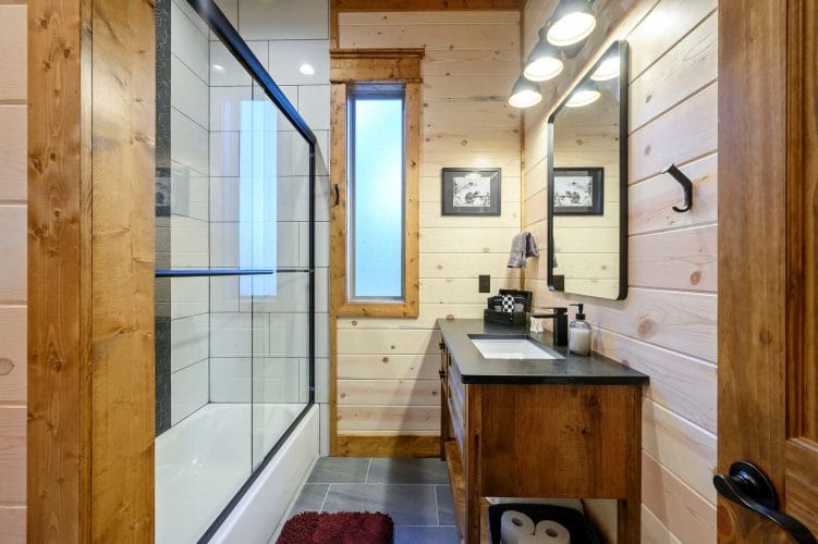 Bathroom vanity with a dark counter beside a narrow window and a glass shower