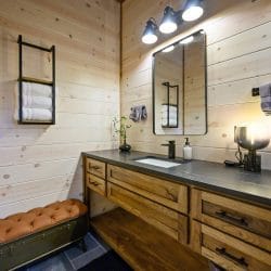 Bathroom vanity with a dark counter, round mirror and shelved towels