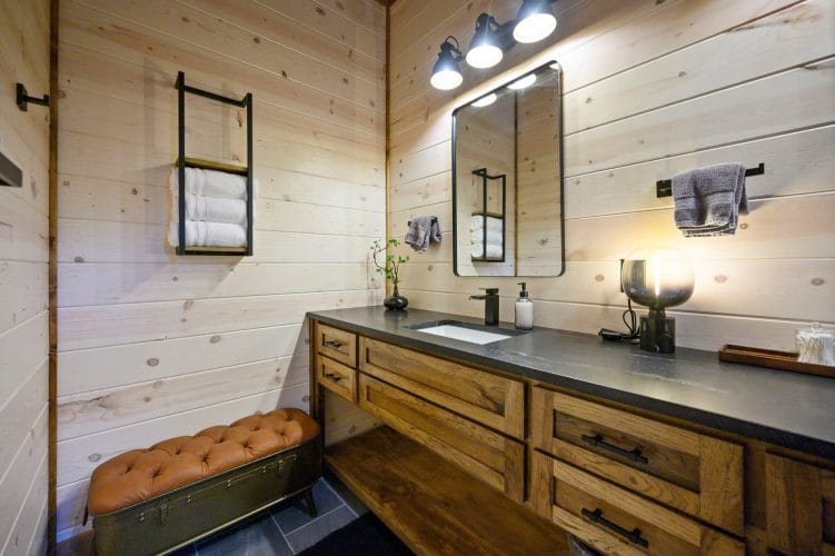 Bathroom vanity with a dark counter, round mirror and shelved towels
