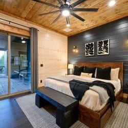 Bed with a wood headboard, black pillows and a black throw against a dark shiplap wall