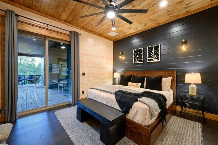 Bed with a wood headboard, black pillows and a black throw against a dark shiplap wall