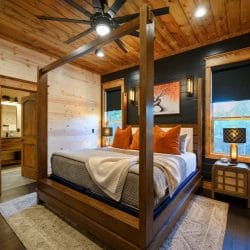 Bed with a wood four-post frame, orange pillows and a window beside a dark shiplap wall
